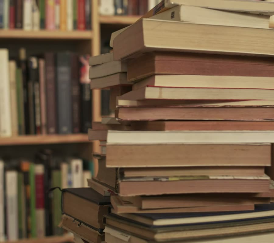 A tall stack of used books in front of full bookshop shelves