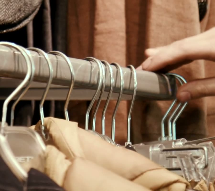 A hand sliding hangers along a rack of second-hand clothes
